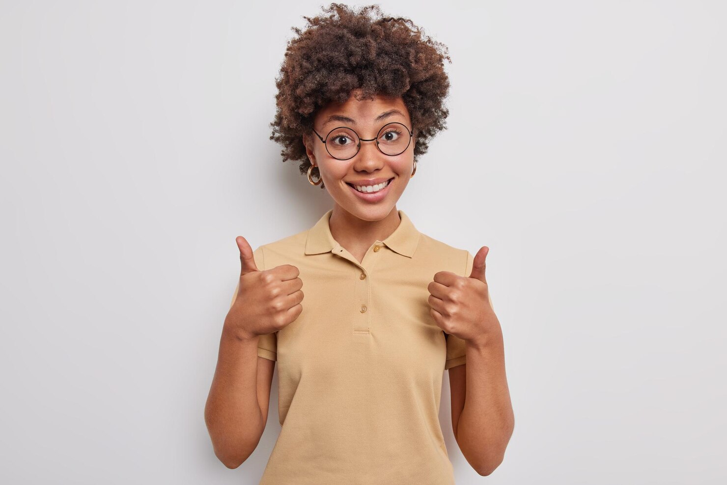 cheerful-curly-girl-keeps-thumbs-up-expresses-like-positive-feedback-approves-supports-plan-praises-store-sale-wears-casual-t-shirt-isolated-white-backgound-celebrates-good-result_273609-56257